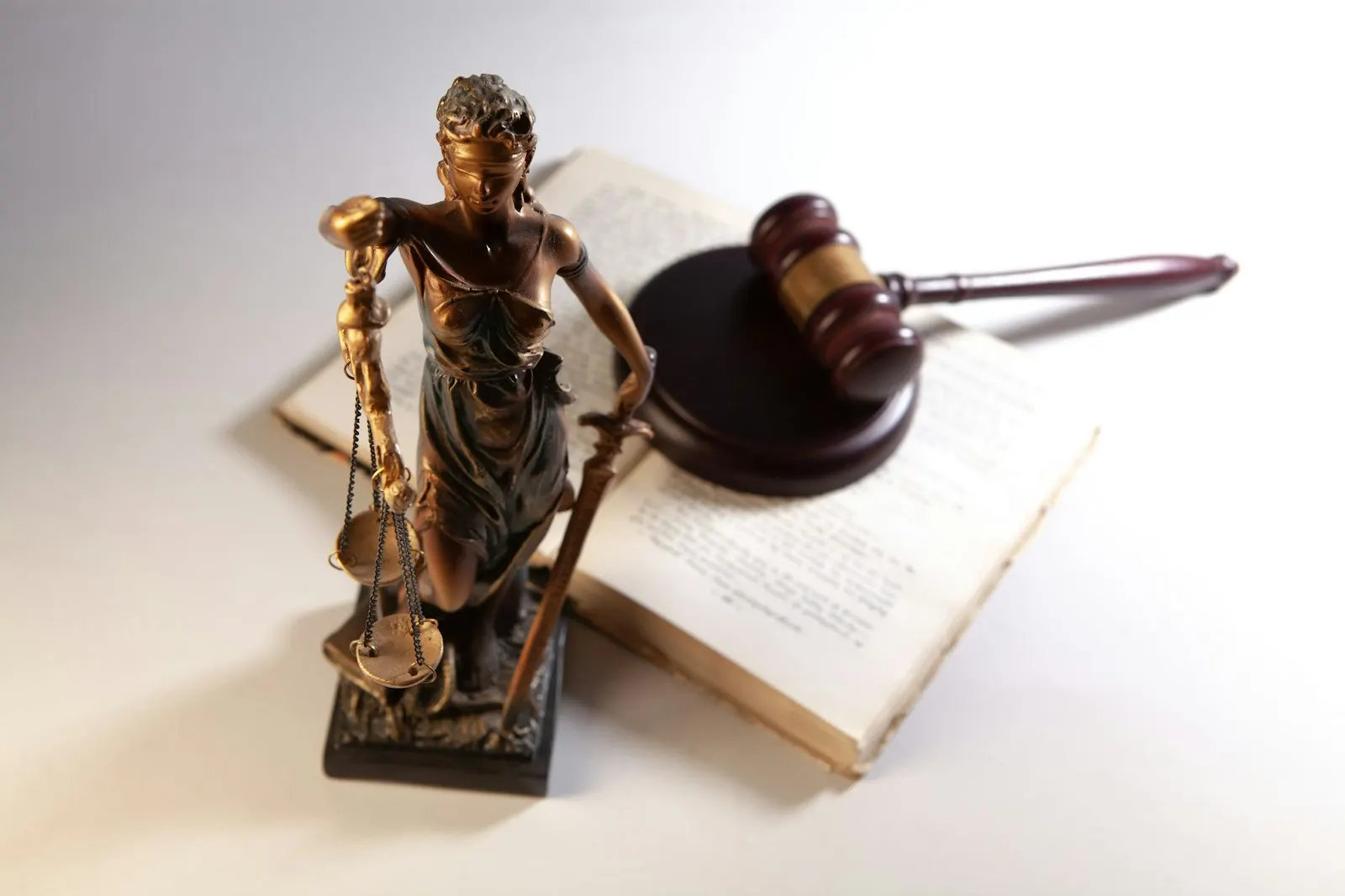 Una piccola statua della Lady Justice che tiene le bilance accanto a un martelletto di legno appoggiato su un libro aperto