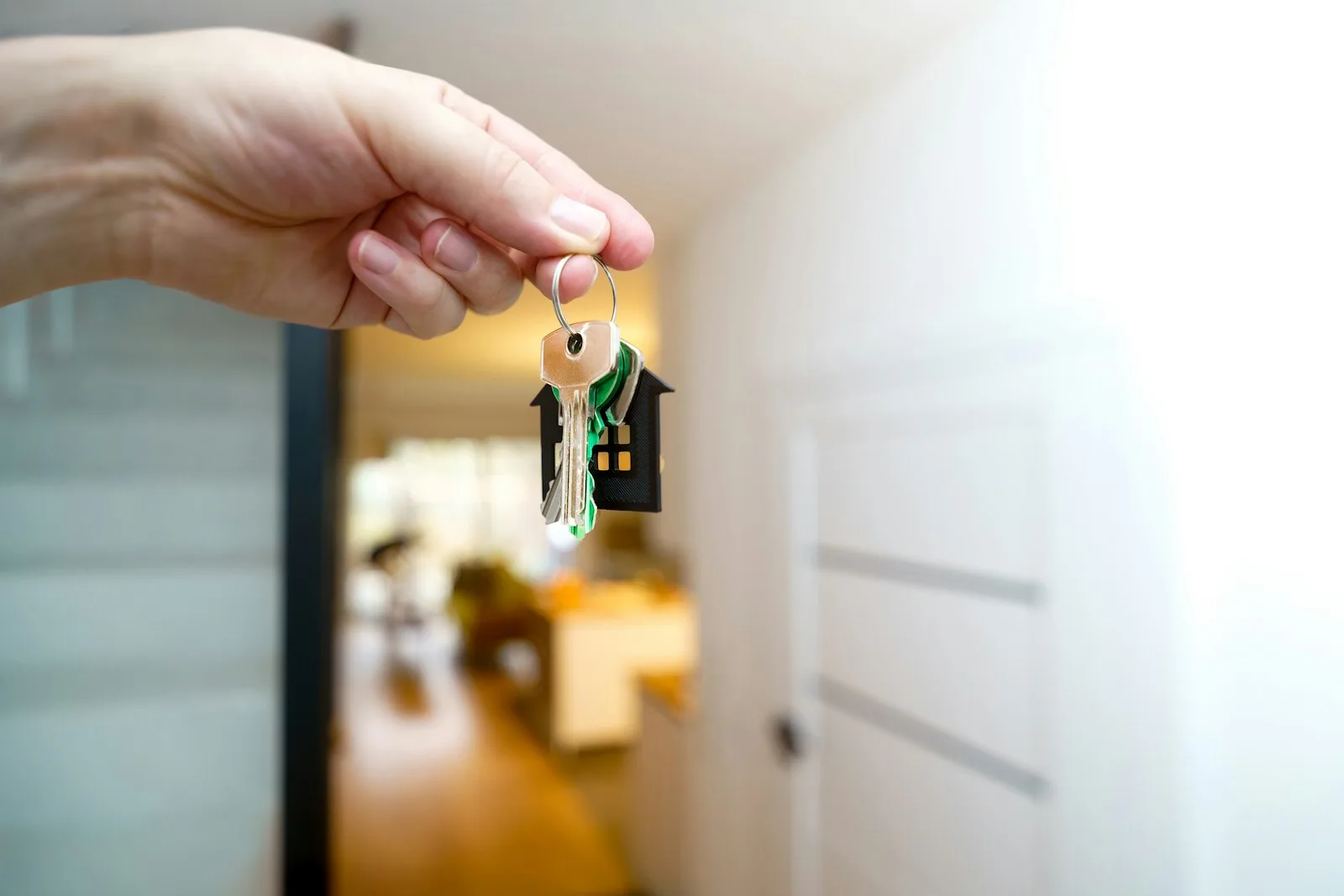 Eine Hand hält einen Satz Hausschlüssel mit einem kleinen hausförmigen Schlüsselanhänger im Eingangsbereich eines neuen Hauses, was einen abgeschlossenen Immobiliendeal symbolisiert